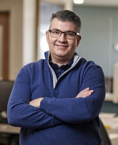 Smiling photo of Dr. Steven LeGrow, arms crossed with clean-cut hair cut, glasses, and wearing half-zip sweater